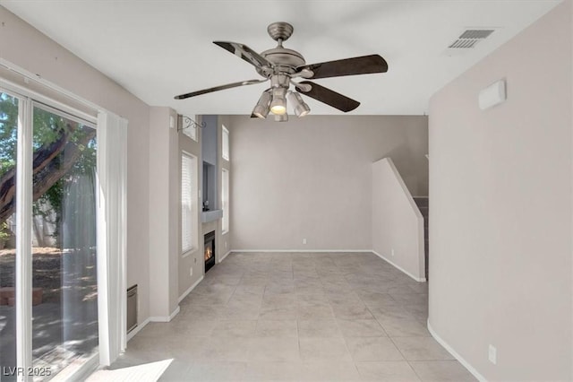 empty room featuring a ceiling fan, a glass covered fireplace, and baseboards