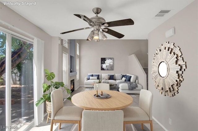 dining area with a ceiling fan, baseboards, and a lit fireplace