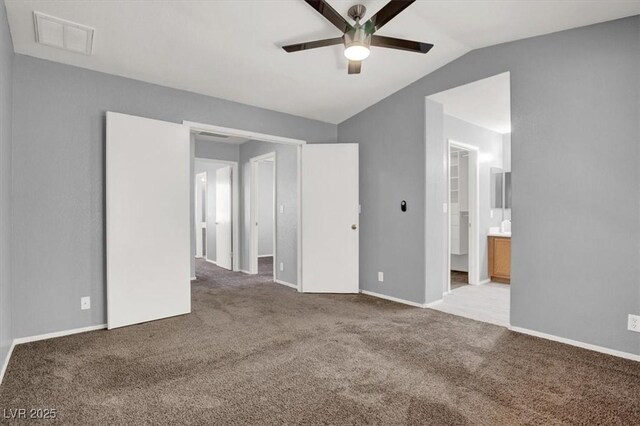unfurnished bedroom featuring lofted ceiling, carpet, ensuite bath, baseboards, and ceiling fan