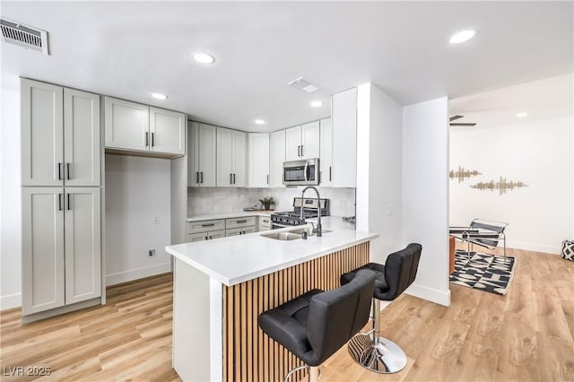 kitchen with stainless steel appliances, a sink, light wood-type flooring, light countertops, and a peninsula