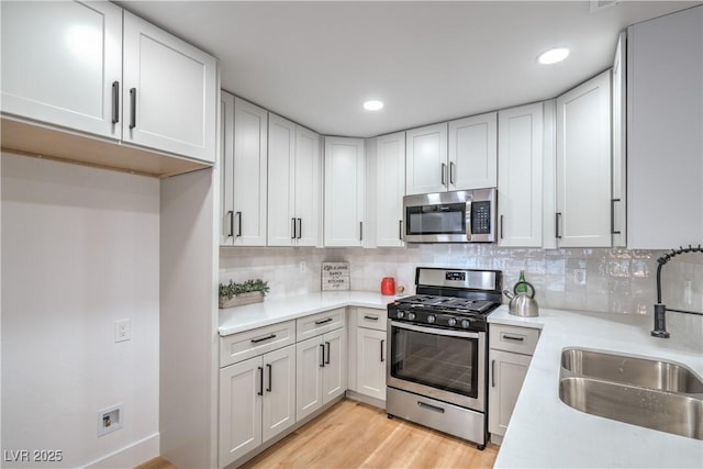 kitchen featuring stainless steel appliances, a sink, light countertops, tasteful backsplash, and light wood-type flooring