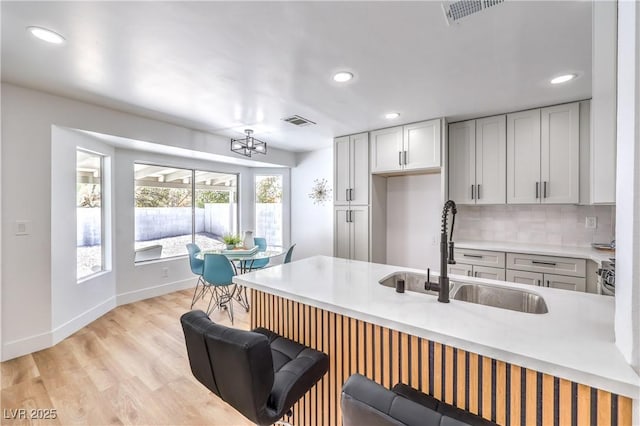 kitchen featuring a sink, light wood finished floors, recessed lighting, tasteful backsplash, and light countertops