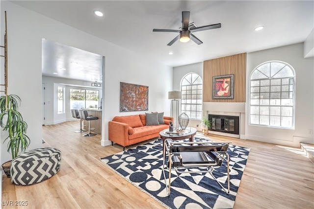 living area with wood finished floors, ceiling fan, baseboards, recessed lighting, and a fireplace