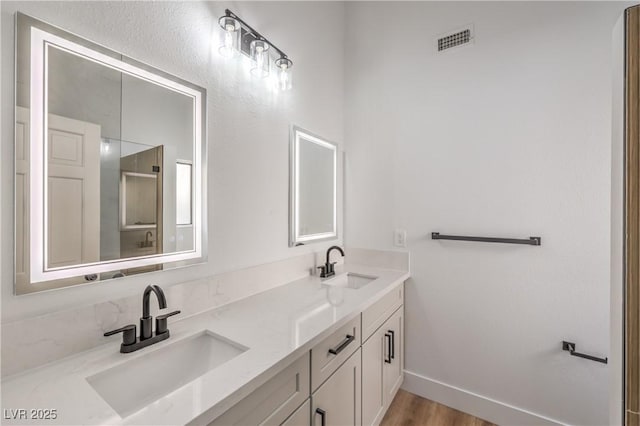 full bath with double vanity, wood finished floors, baseboards, and a shower