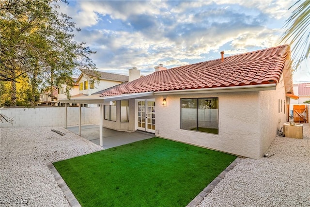 rear view of house with stucco siding, a tiled roof, a chimney, and a patio area