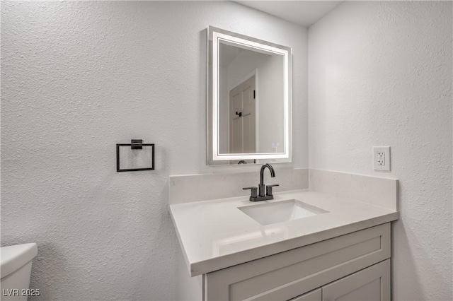 bathroom with toilet, vanity, and a textured wall