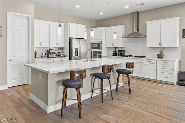kitchen featuring wall chimney exhaust hood, appliances with stainless steel finishes, backsplash, light wood-type flooring, and recessed lighting