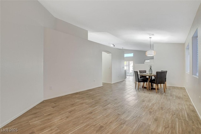 dining space with light wood-style flooring, arched walkways, and baseboards