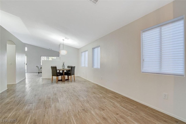 dining room with light wood-style flooring, lofted ceiling, arched walkways, and baseboards
