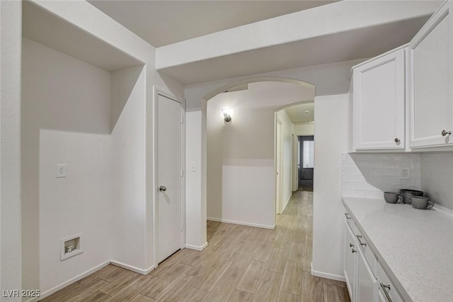 kitchen featuring light countertops, light wood finished floors, white cabinets, arched walkways, and tasteful backsplash