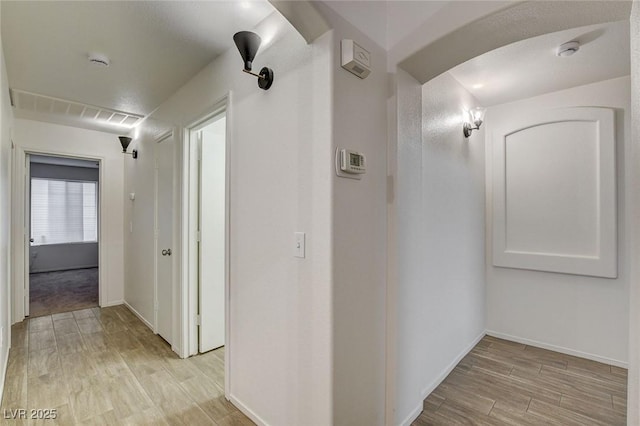 hallway featuring light wood-style flooring, baseboards, and arched walkways