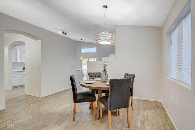 dining space with light wood-style floors, baseboards, arched walkways, and vaulted ceiling