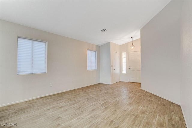 empty room featuring light wood finished floors, vaulted ceiling, and baseboards