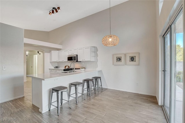 kitchen featuring stainless steel microwave, high vaulted ceiling, a kitchen breakfast bar, a peninsula, and arched walkways