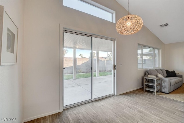 doorway to outside featuring light wood finished floors, high vaulted ceiling, and baseboards