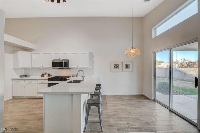 kitchen featuring stainless steel microwave, a sink, gas range, a towering ceiling, and a breakfast bar area