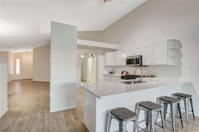 kitchen featuring stainless steel microwave, open shelves, light countertops, light wood-type flooring, and a peninsula