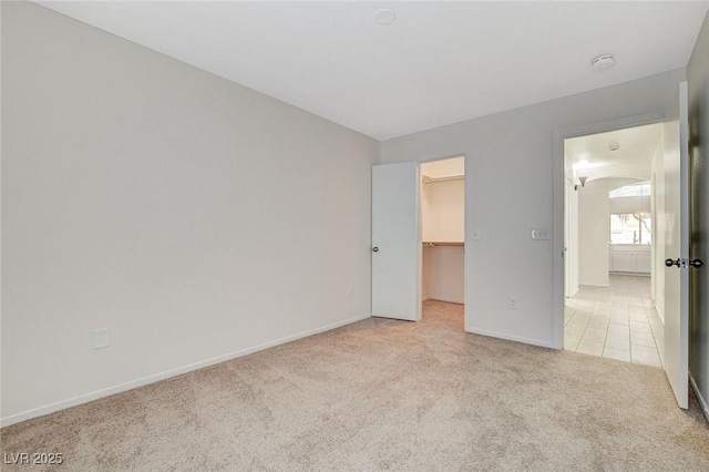 unfurnished bedroom featuring light colored carpet, a spacious closet, baseboards, and a closet