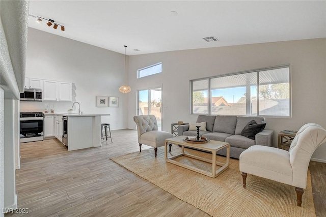 living room with light wood-style flooring, high vaulted ceiling, and track lighting