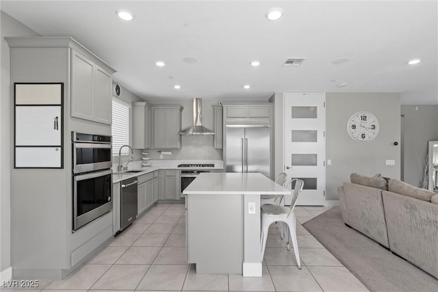 kitchen with wall chimney exhaust hood, stainless steel appliances, a sink, open floor plan, and a breakfast bar