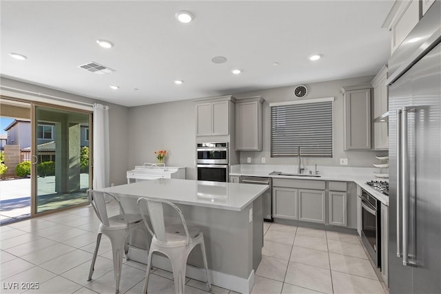 kitchen featuring a sink, gray cabinetry, appliances with stainless steel finishes, a center island, and light countertops