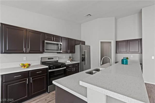556 Decidedly St, Henderson, NV 89015 - kitchen with stainless steel appliances, light wood-type flooring, an island with sink, a towering ceiling, and dark brown cabinetry