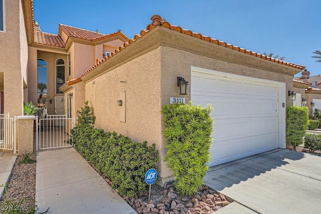 view of side of home with stucco siding, driveway, a tile roof, and a garage