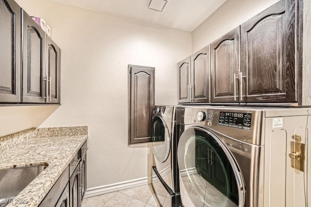 clothes washing area featuring cabinet space, washer and dryer, light tile patterned floors, and baseboards