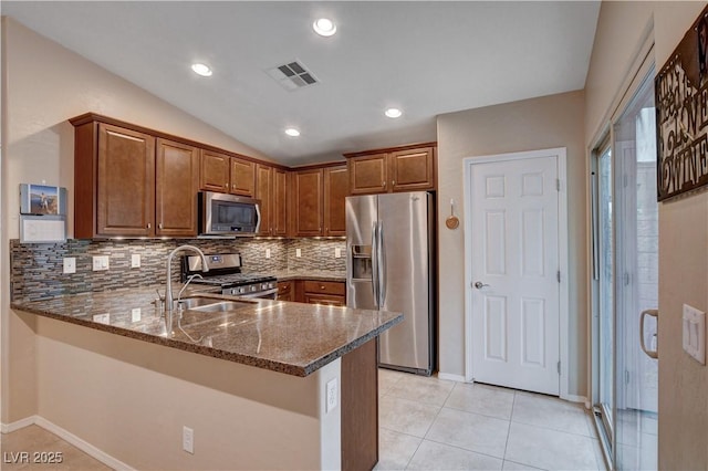 3712 Rocklin Peak Ave, North Las Vegas, NV 89081 - kitchen with appliances with stainless steel finishes, a sink, dark stone countertops, decorative backsplash, and brown cabinets