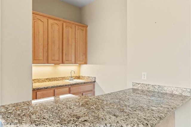kitchen featuring a sink, light brown cabinets, light stone counters, and a peninsula