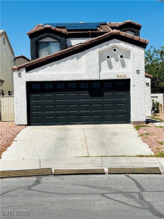 view of front of house featuring a tile roof, a garage, concrete driveway, roof mounted solar panels, and stucco siding