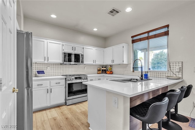 kitchen with stainless steel appliances, a peninsula, light wood-style flooring, a sink, and a breakfast bar