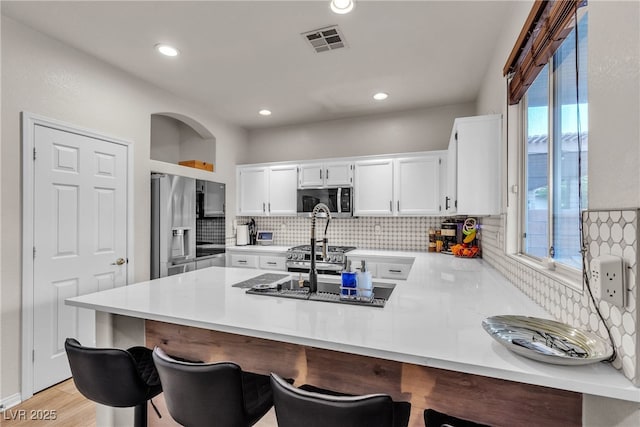 kitchen featuring appliances with stainless steel finishes, a peninsula, tasteful backsplash, light countertops, and white cabinets