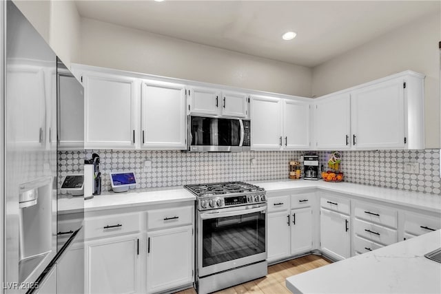 kitchen featuring appliances with stainless steel finishes, white cabinets, light wood-style floors, and backsplash
