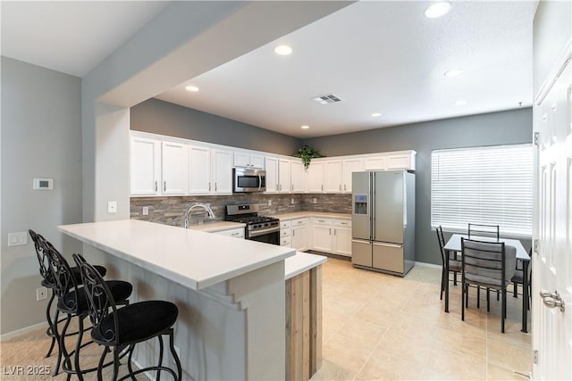 kitchen with appliances with stainless steel finishes, backsplash, a kitchen bar, a peninsula, and light countertops