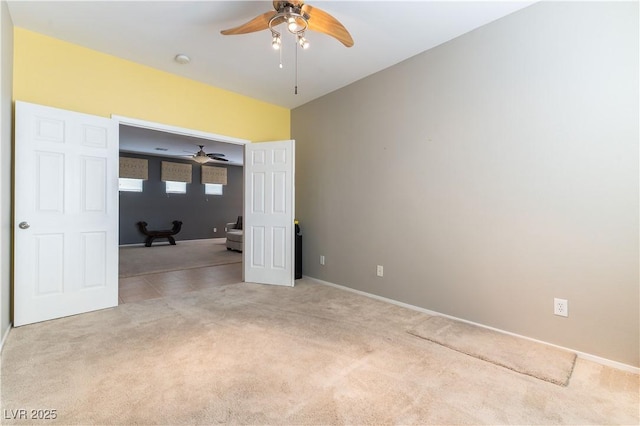 empty room featuring a ceiling fan, light colored carpet, baseboards, and a smoke detector