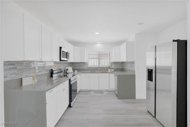 kitchen featuring appliances with stainless steel finishes, a sink, backsplash, white cabinetry, and light wood-style floors