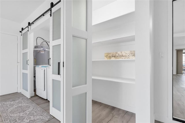 detailed view of a barn door, washer / dryer, wood finished floors, and water heater