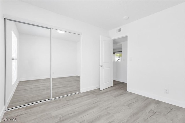 unfurnished bedroom featuring wood finished floors, baseboards, and a closet