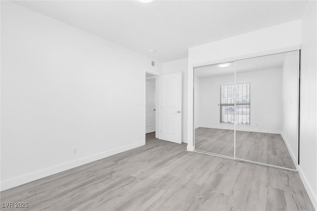 unfurnished bedroom featuring wood finished floors, baseboards, and a closet