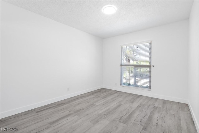 empty room featuring a textured ceiling, wood finished floors, and baseboards