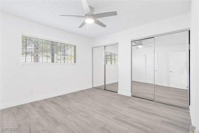 unfurnished bedroom featuring two closets, wood finished floors, baseboards, and a ceiling fan