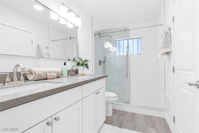 bathroom featuring a shower stall, toilet, double vanity, and wood finished floors