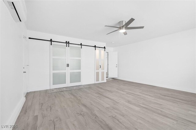 spare room with an AC wall unit, wood finished floors, ceiling fan, a barn door, and baseboards
