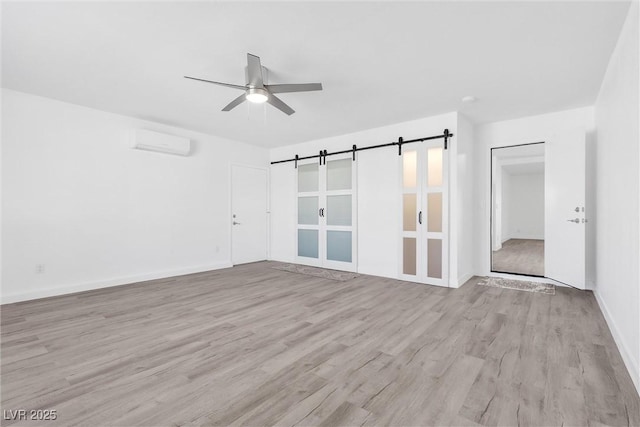 unfurnished room featuring a wall mounted air conditioner, a ceiling fan, light wood-type flooring, and a barn door
