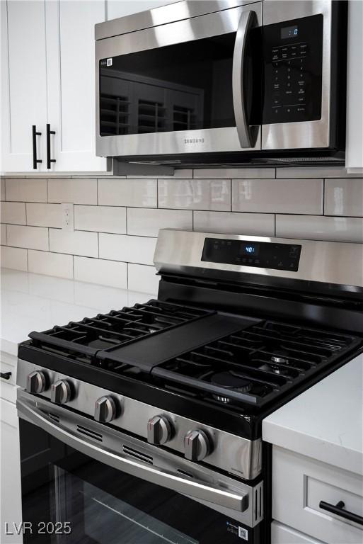 kitchen view of stainless steel appliances, white cabinetry, tasteful backsplash, and light countertops