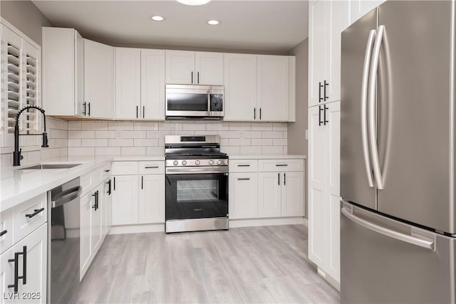 kitchen featuring appliances with stainless steel finishes, a sink, light countertops, backsplash, and recessed lighting