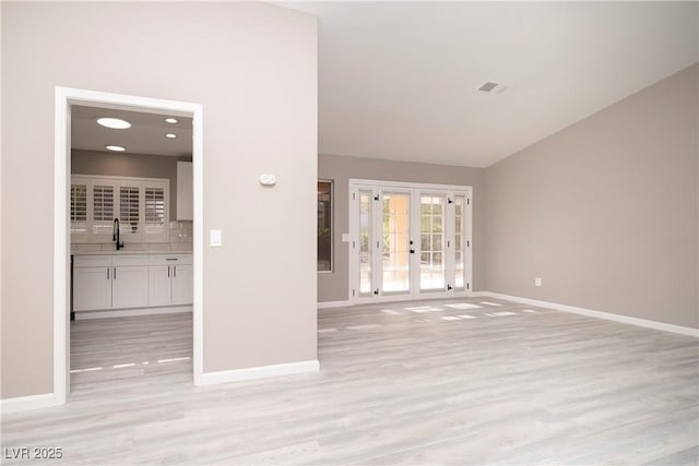 unfurnished living room with light wood-style floors, baseboards, french doors, and vaulted ceiling