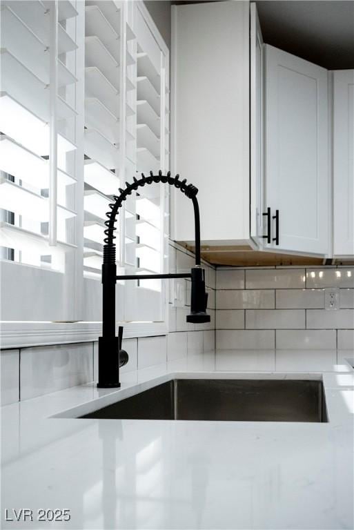 kitchen view of backsplash, a sink, white cabinetry, and light countertops