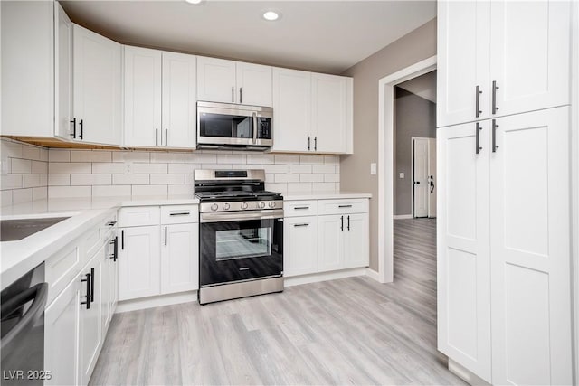 kitchen with appliances with stainless steel finishes, light wood-style flooring, light countertops, backsplash, and baseboards